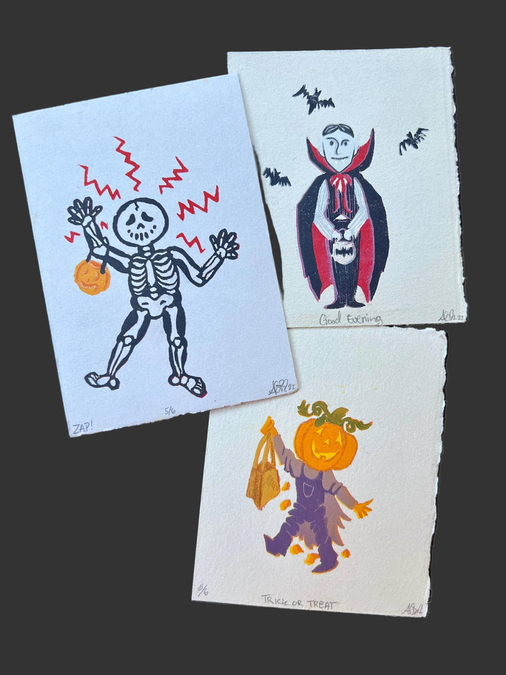 Three Halloween-themed prints featuring a skeleton, vampire, and pumpkin character on a dark surface.