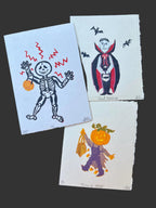 Three Halloween-themed prints featuring a skeleton, vampire, and pumpkin character on a dark surface.